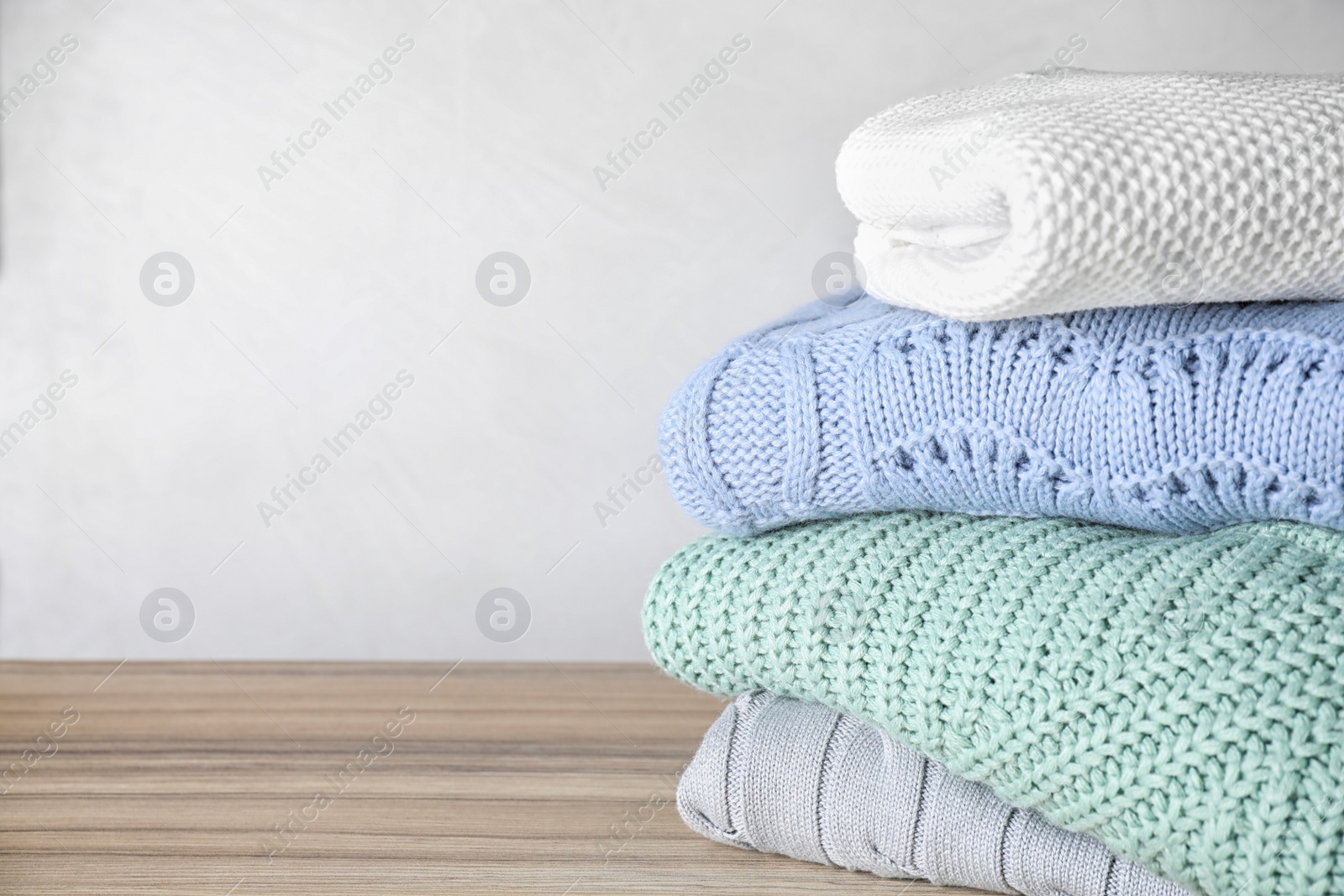 Image of Stack of folded warm sweaters on wooden table. Space for text