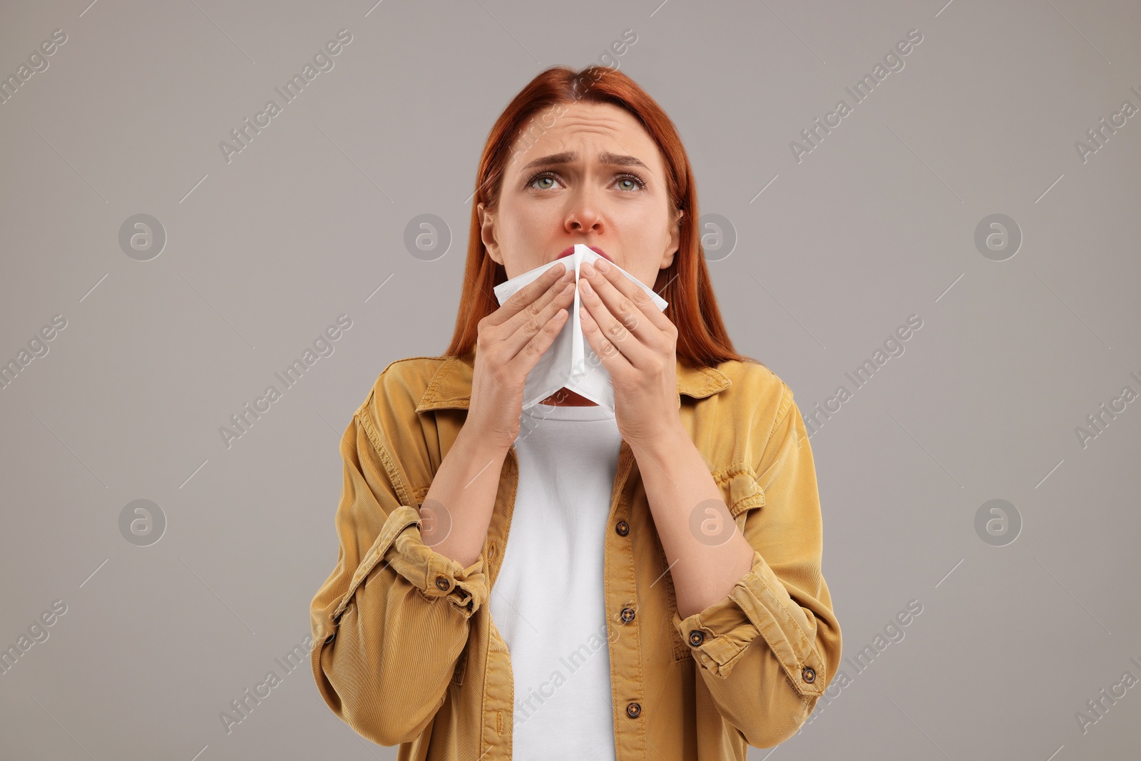 Photo of Suffering from allergy. Young woman with tissue sneezing on grey background