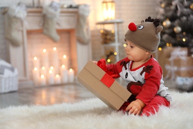 Little baby in festive Christmas costume playing with gift at home