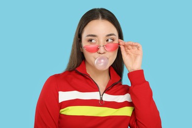 Photo of Beautiful young woman blowing bubble gum on light blue background