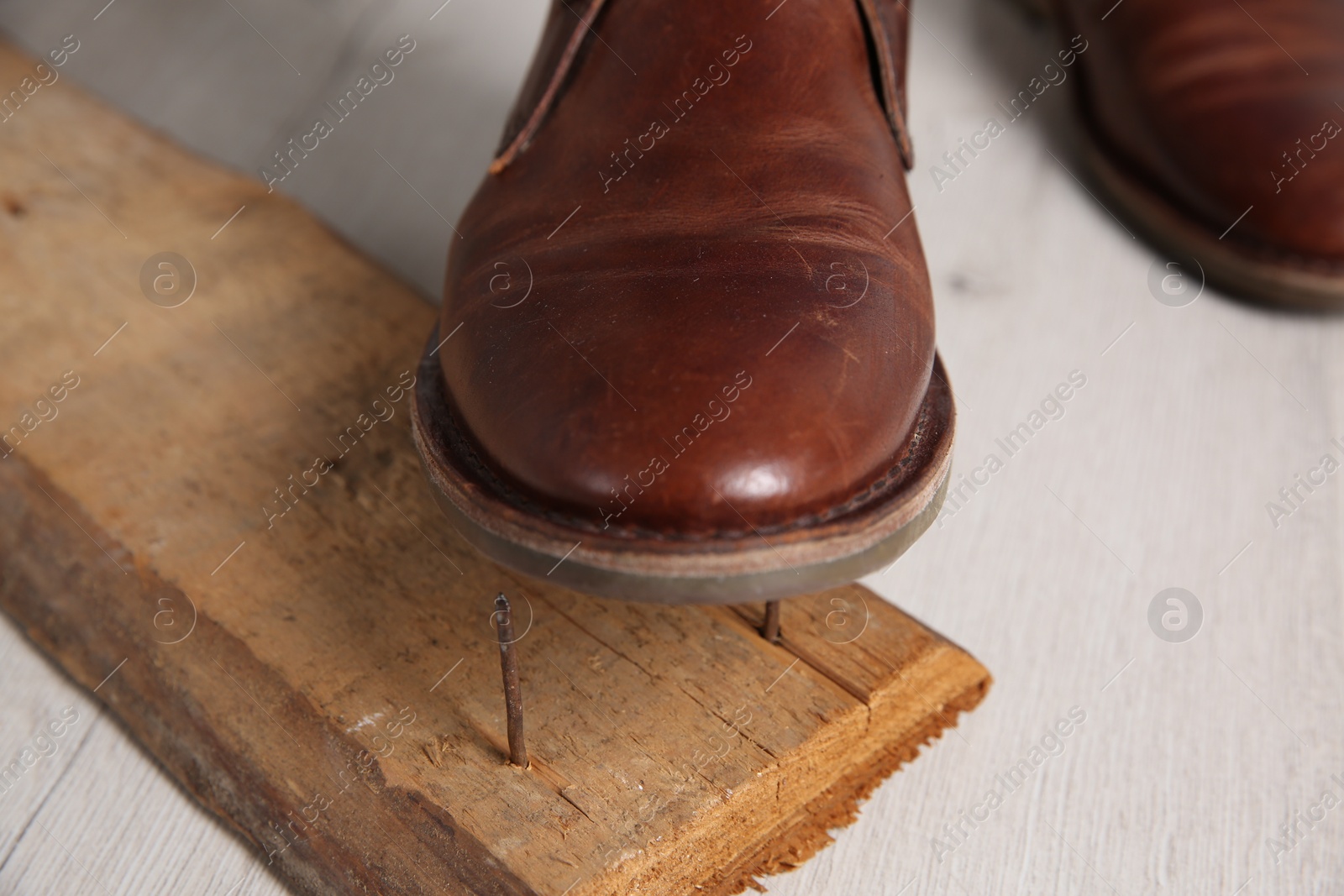 Photo of Careless man stepping on nails in wooden plank, closeup