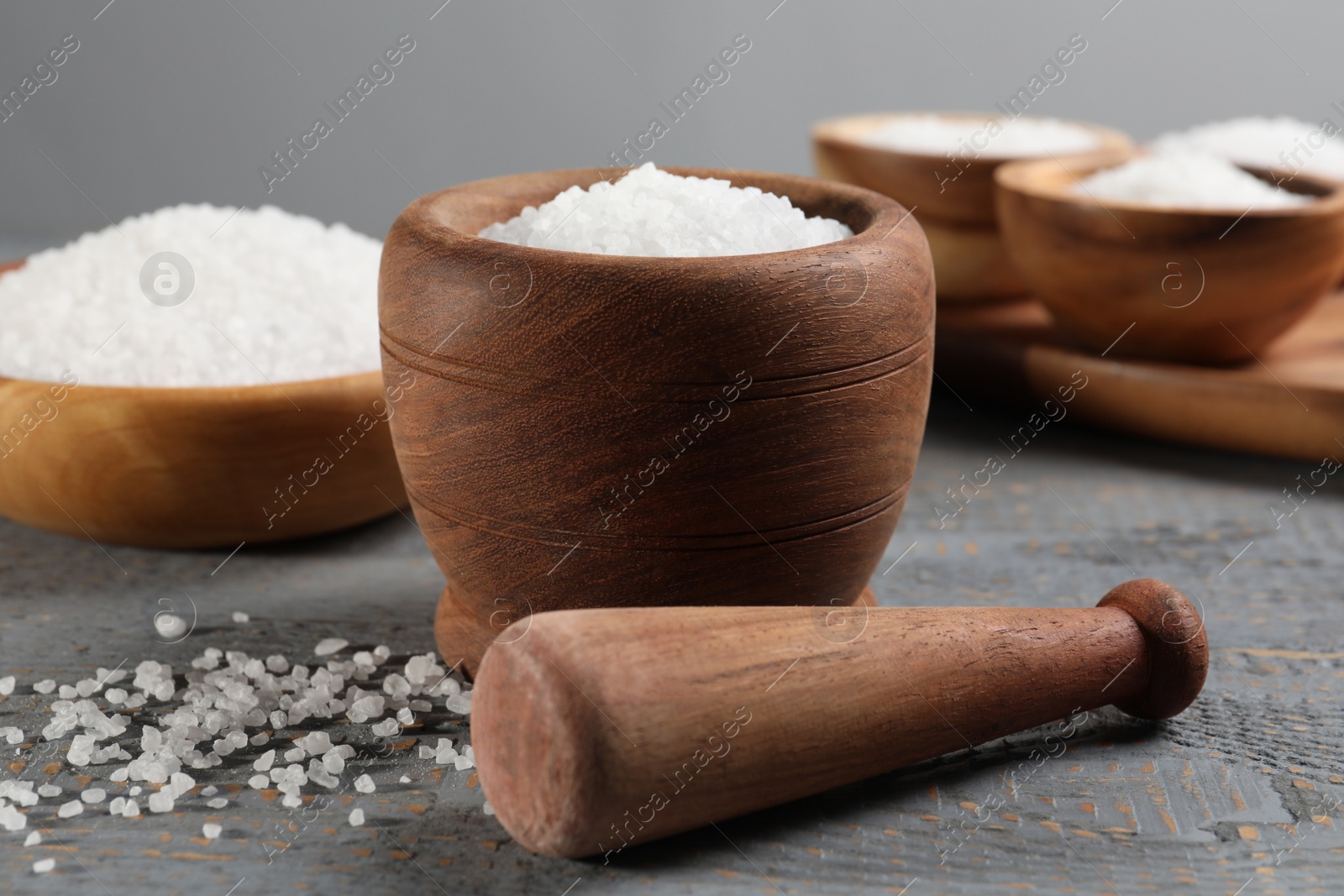 Photo of Pestle and mortar with natural sea salt on grey wooden table