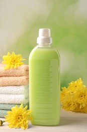 Photo of Bottle of laundry detergent, towels and beautiful flowers on white table