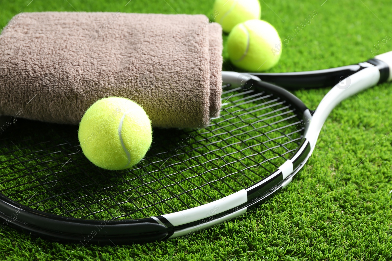 Photo of Tennis racket, towel and balls on green grass, closeup. Sports equipment