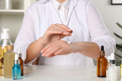 Photo of Dermatologist testing cosmetic product at white table indoors, closeup