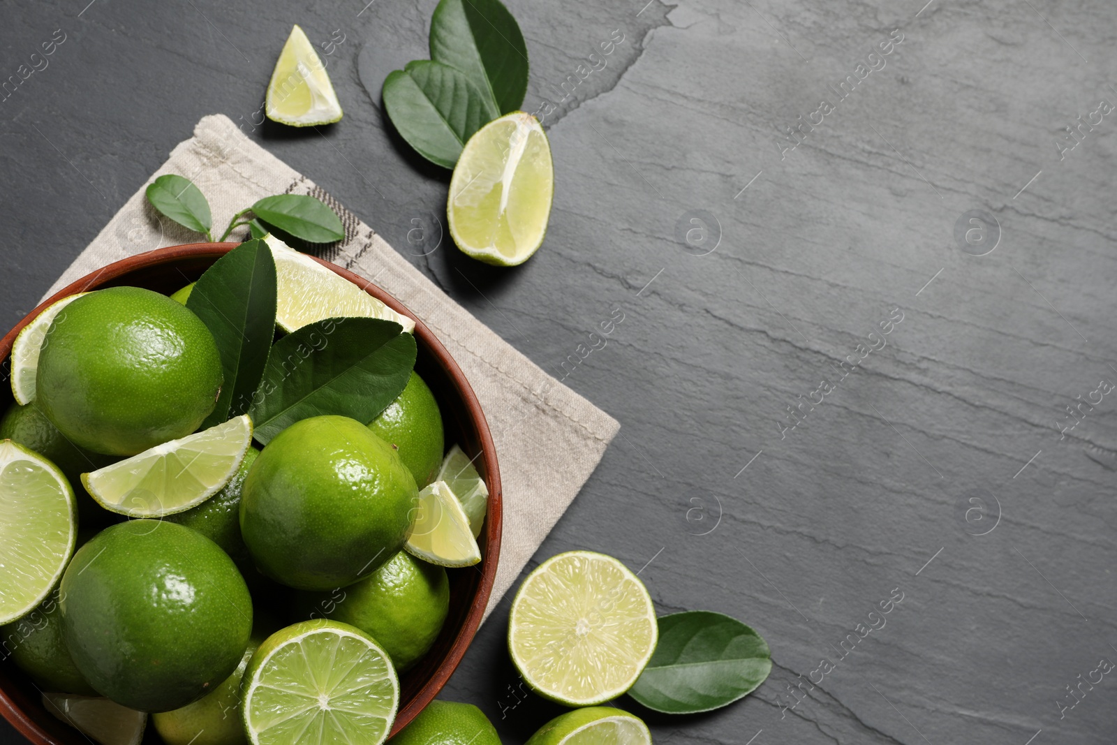 Photo of Fresh ripe limes in bowl on black table, top view. Space for text