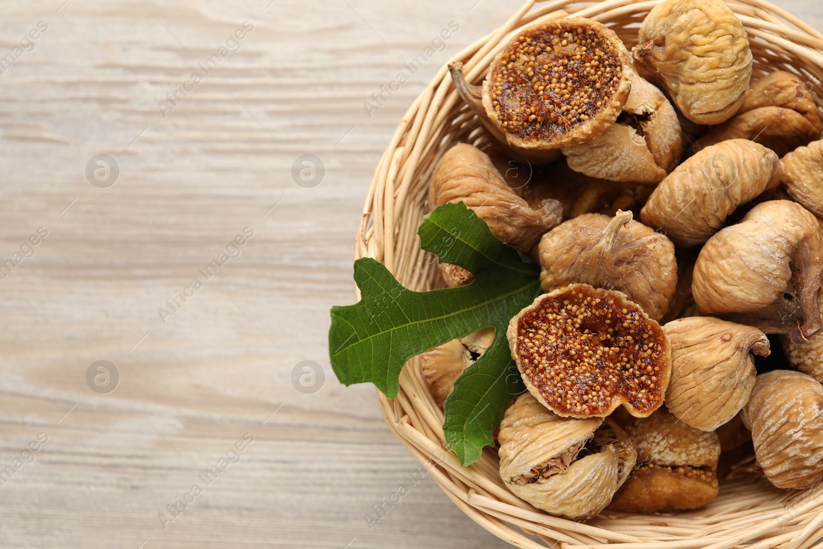 Photo of Wicker basket with tasty dried figs and green leaf on light wooden table, top view. Space for text