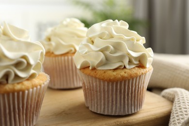 Photo of Tasty cupcakes with vanilla cream on wooden board, closeup