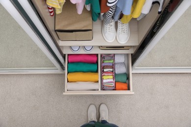 Photo of Woman near wardrobe with organized clothes and shoes indoors, top view. Vertical storage