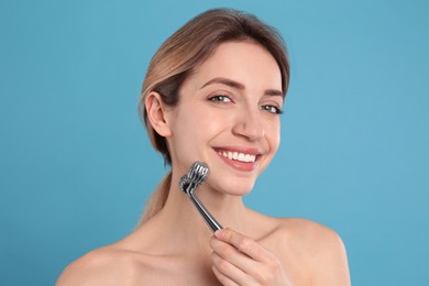 Young woman using metal face roller on light blue background