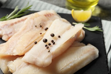 Photo of Pieces of raw cod fish and peppercorns on table, closeup