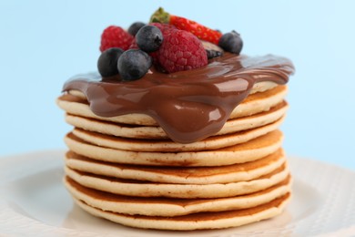 Photo of Stack of tasty pancakes with fresh berries and chocolate spread on light blue background, closeup