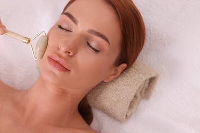 Photo of Young woman receiving facial massage with jade roller in beauty salon, above view. Space for text