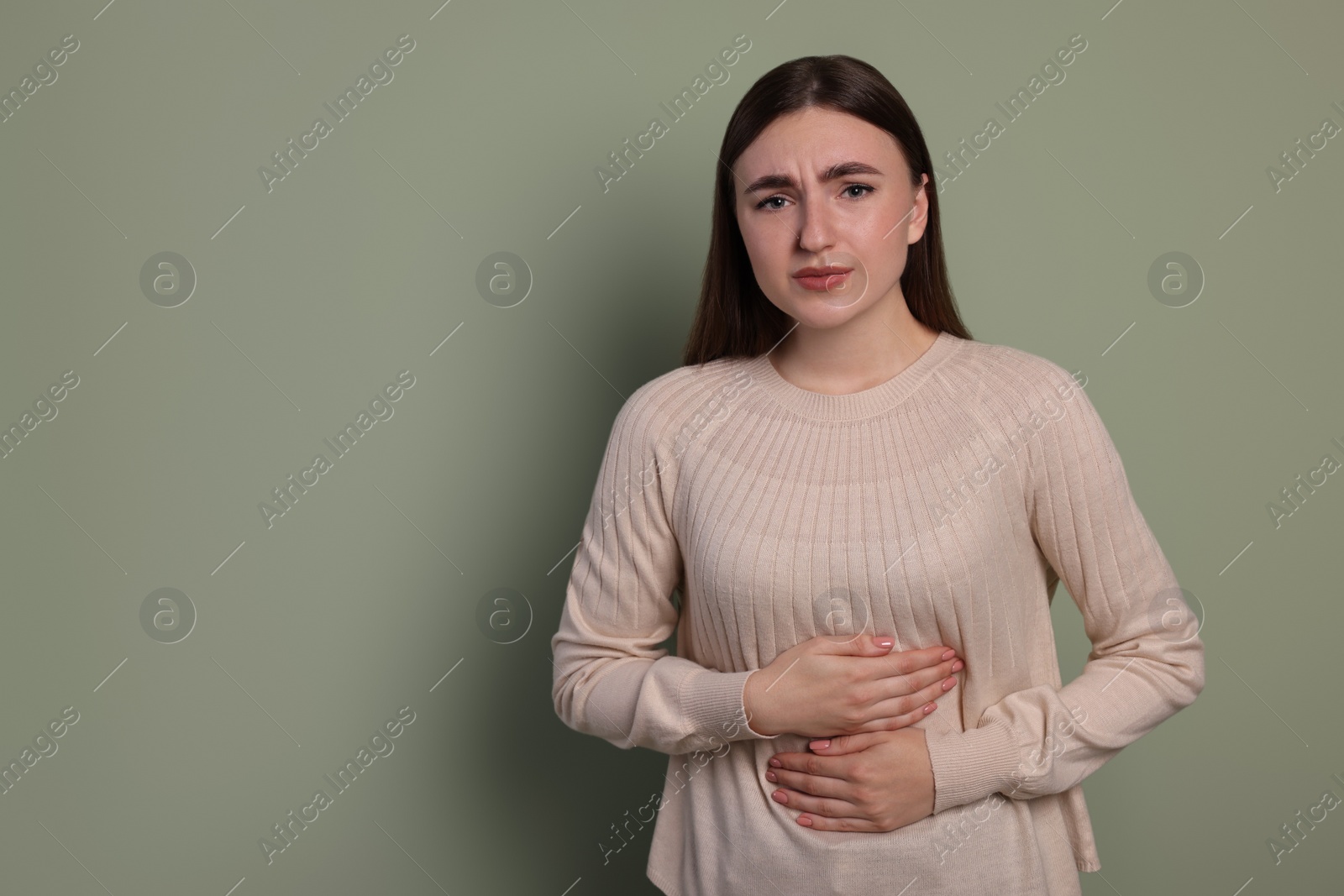 Photo of Young woman suffering from stomach pain on green background. Space for text