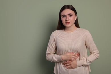 Young woman suffering from stomach pain on green background. Space for text
