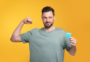 Photo of Handsome man holding condom on orange background
