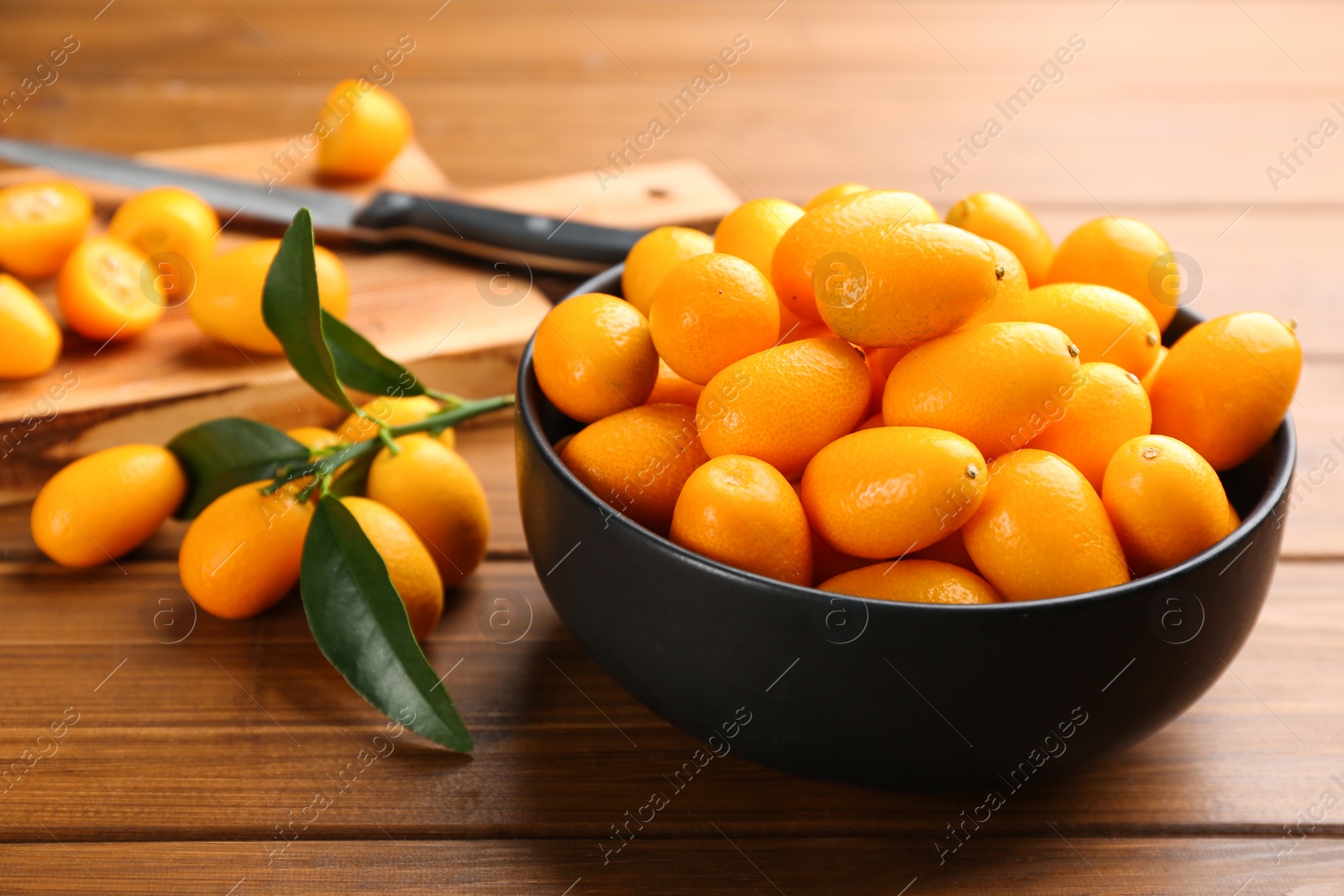 Photo of Fresh ripe kumquats with green leaves on wooden table