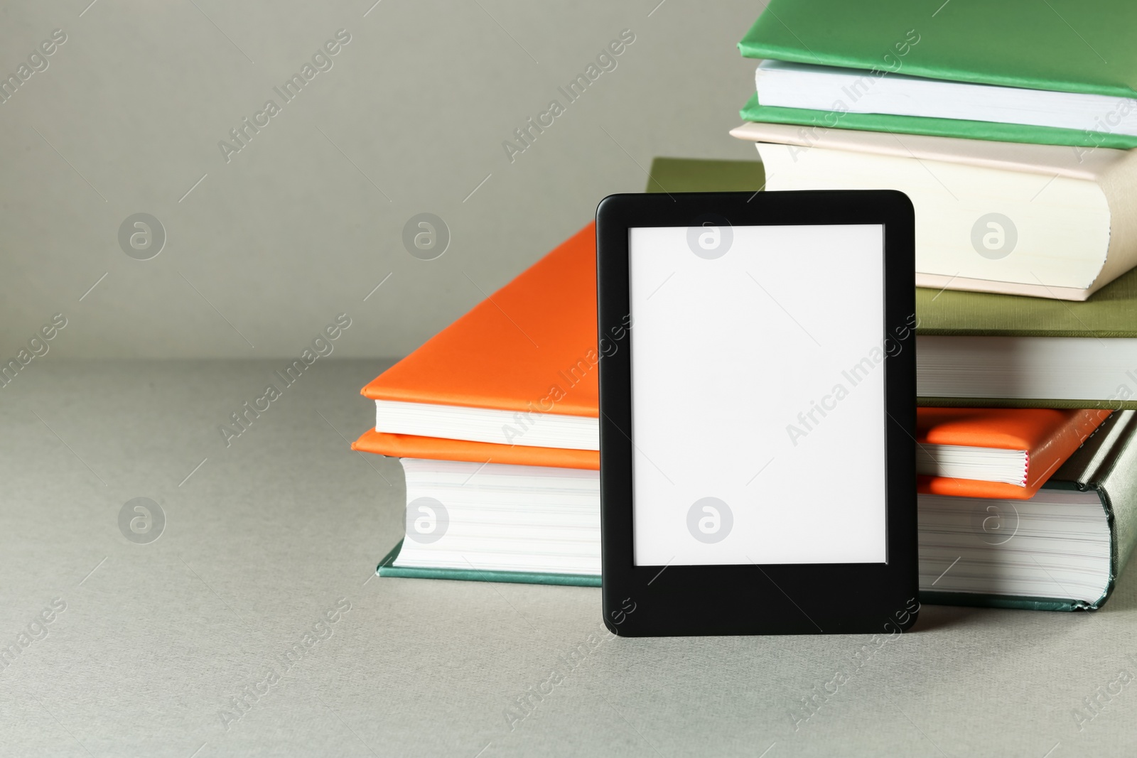 Photo of Modern e-book reader and stack of hard cover books on light grey table. Space for text