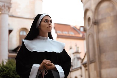 Photo of Beautiful young nun in cassock near building outdoors
