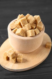 Photo of Brown sugar cubes in bowl on black wooden table, closeup