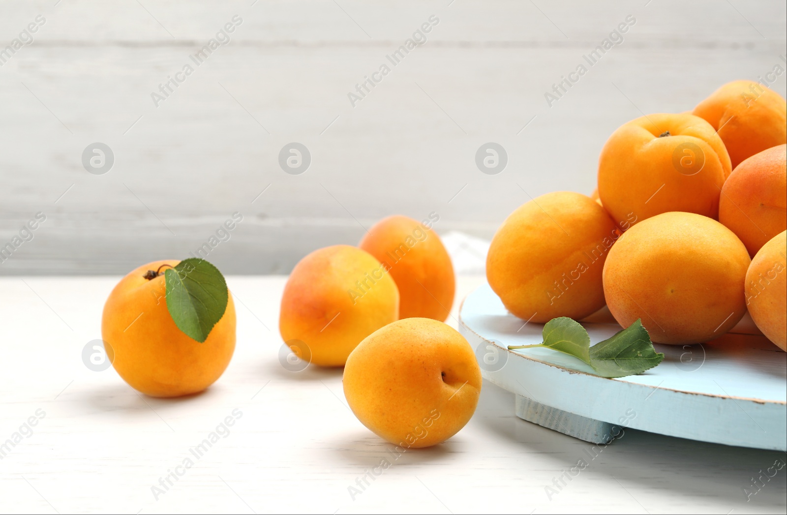 Photo of Delicious ripe sweet apricots and board on white wooden table, space for text