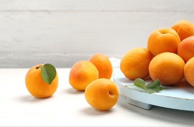 Delicious ripe sweet apricots and board on white wooden table, space for text