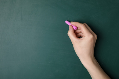 Woman with pink chalk near green blackboard, closeup. Space for text