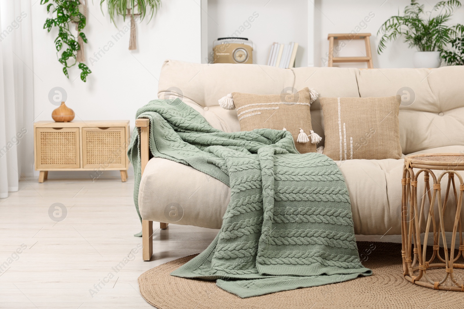 Photo of Comfortable sofa, blanket and side table in living room