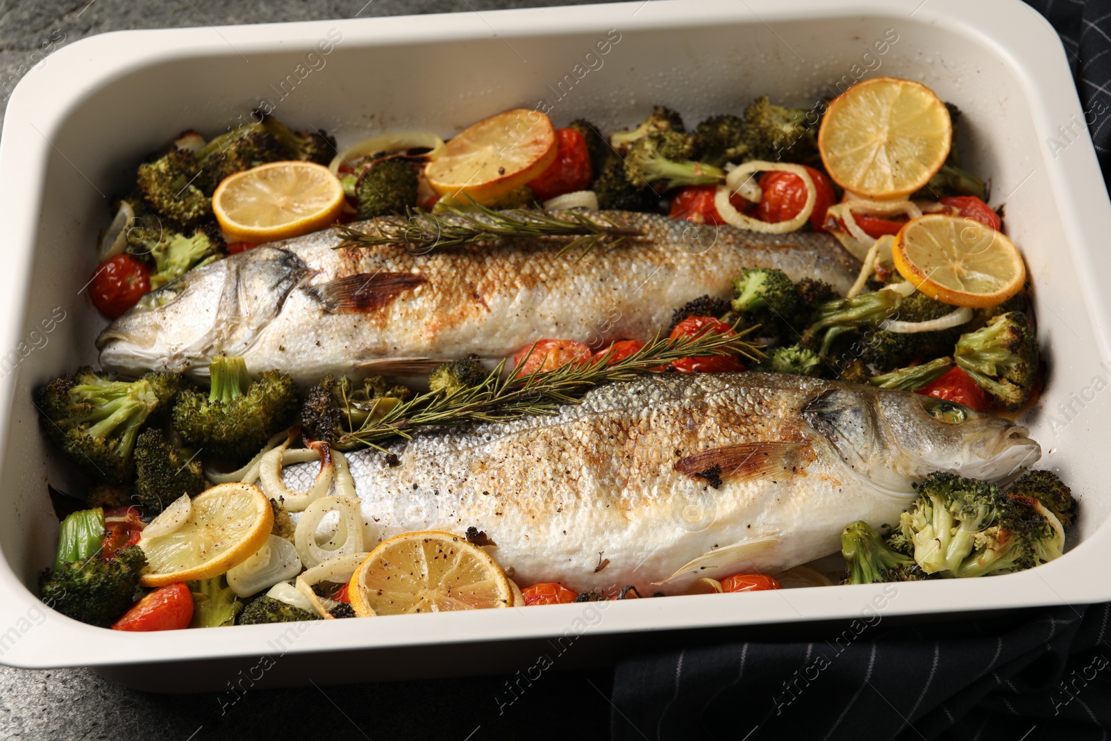 Photo of Delicious fish with vegetables and lemon in baking dish on table