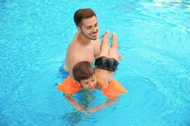 Father teaching son to swim with inflatable sleeves in pool