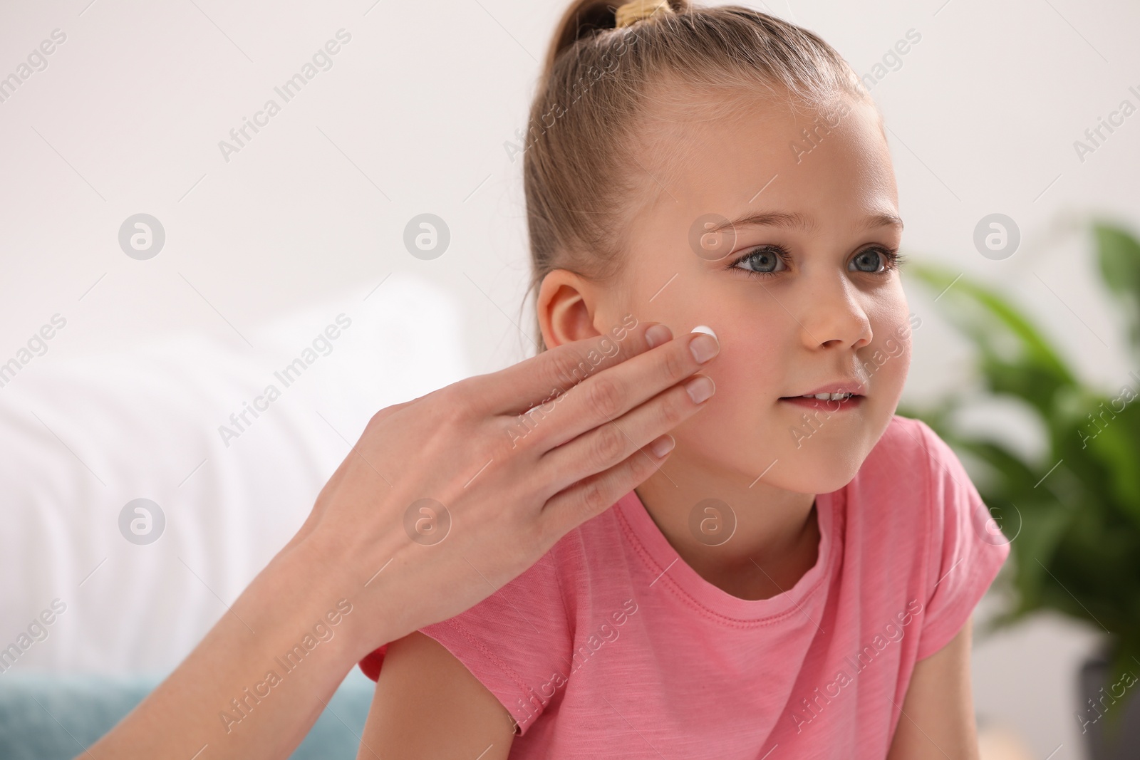 Photo of Mother applying ointment onto her daughter's cheek indoors