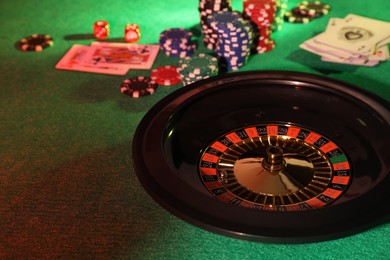 Photo of Roulette wheel with ball, playing cards and chips on green table. Casino game
