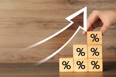 Image of Mortgage rate rising illustrated by upward arrow. Woman putting cube with percent sign on other ones at wooden table, closeup