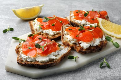 Delicious sandwiches with cream cheese, salmon and microgreens on light grey table, closeup