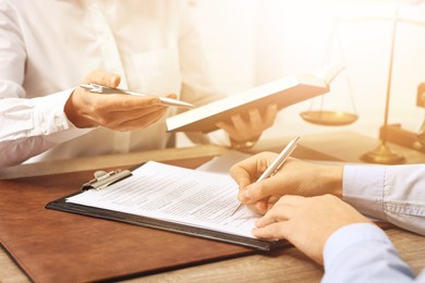 Image of Lawyer working with client at wooden table in office, closeup