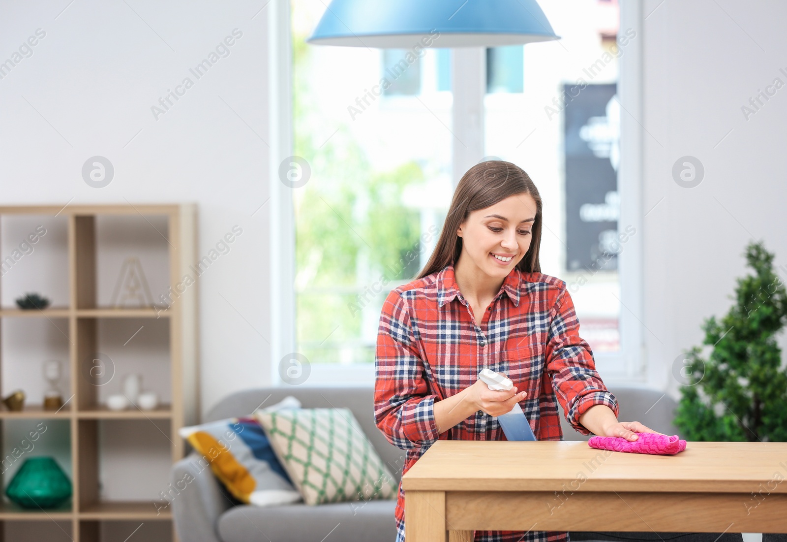 Photo of Young woman cleaning table with rag indoors