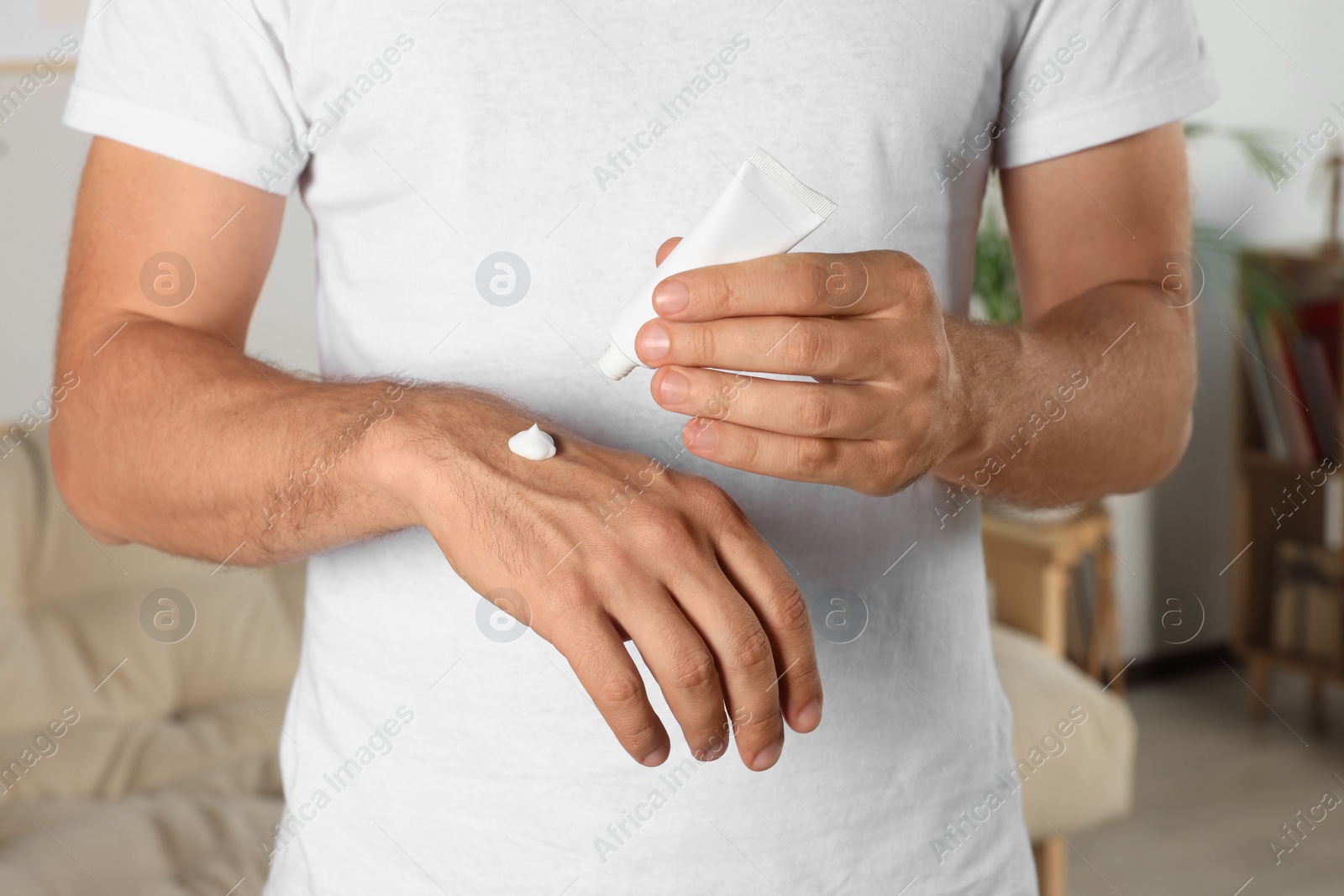 Photo of Man applying cream from tube onto hand at home, closeup