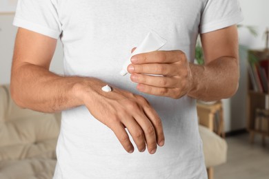 Photo of Man applying cream from tube onto hand at home, closeup