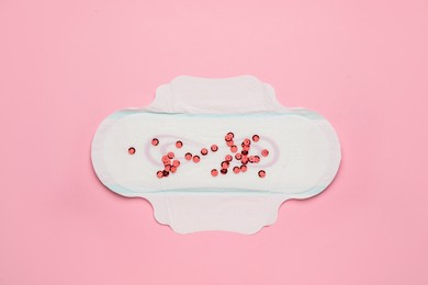 Menstrual pad with red sequins on pink background, top view