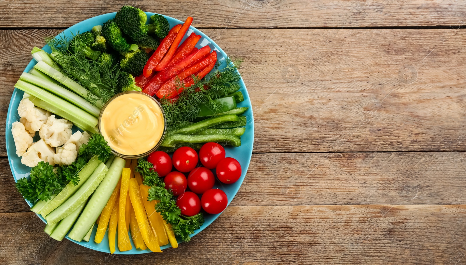 Photo of Celery and other vegetable sticks with dip sauce on wooden table, top view. Space for text