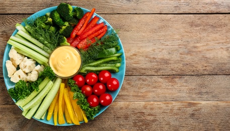 Celery and other vegetable sticks with dip sauce on wooden table, top view. Space for text