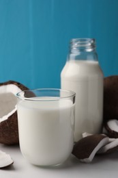 Glass and bottle of delicious vegan milk near coconut pieces on white table