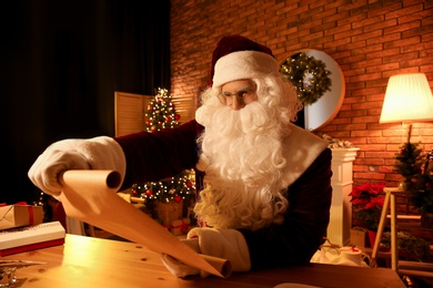 Photo of Santa Claus reading wish list at table indoors