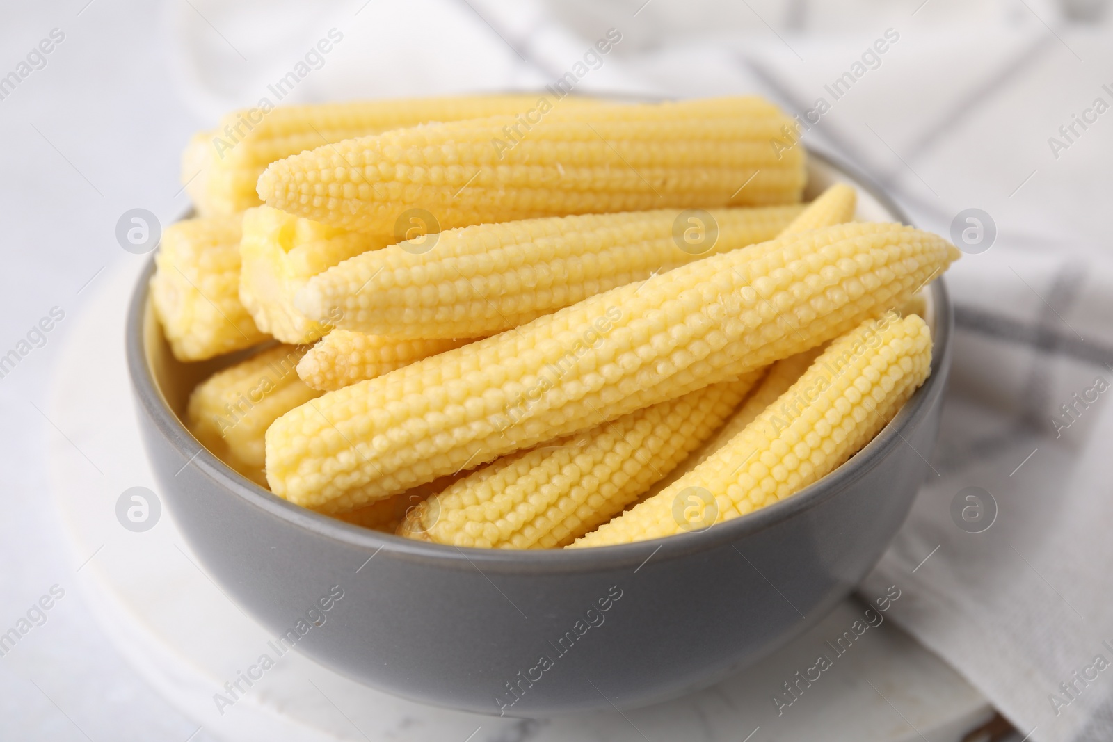 Photo of Tasty fresh yellow baby corns in bowl on white table, closeup