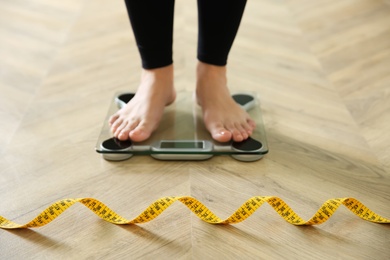 Photo of Woman with measuring tape standing on scales indoors, closeup. Overweight problem