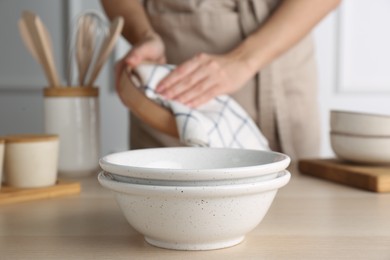 Woman wiping dishware with towel indoors, focus on clean bowls