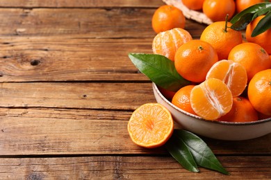 Fresh tangerines with green leaves in bowl on wooden table, space for text