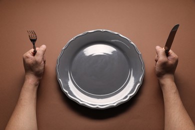 Photo of Man with cutlery and empty plate at brown table, above view