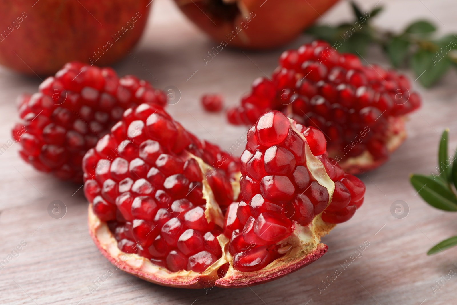 Photo of Cut fresh pomegranate and green leaves on wooden table, closeup