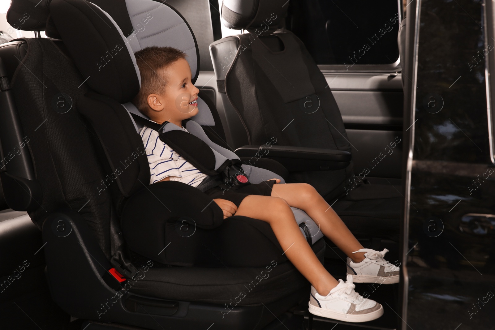 Photo of Little boy fastened with car safety belt in child seat